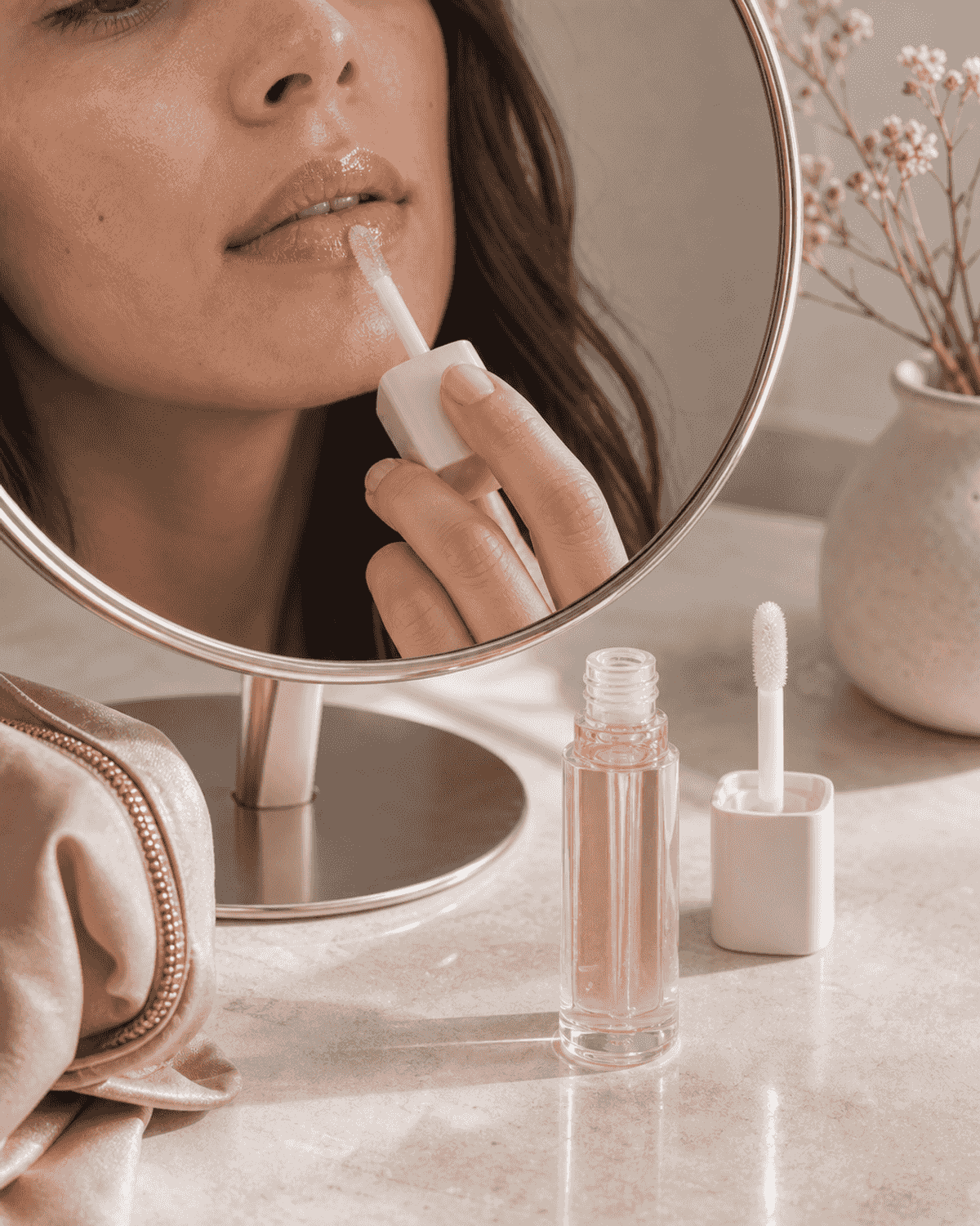 A tinted lip oil tube beside a compact mirror and soft cloth.