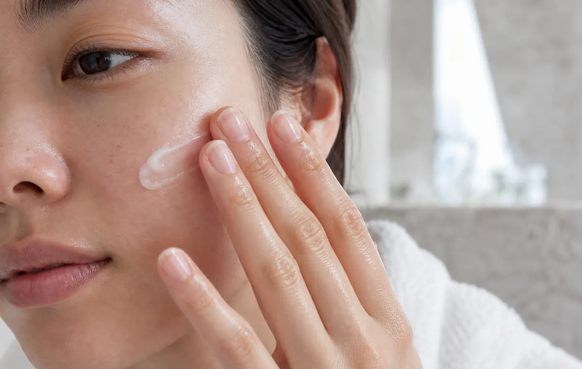 Fingertips pressing moisturizer into the cheek in soft bathroom light.