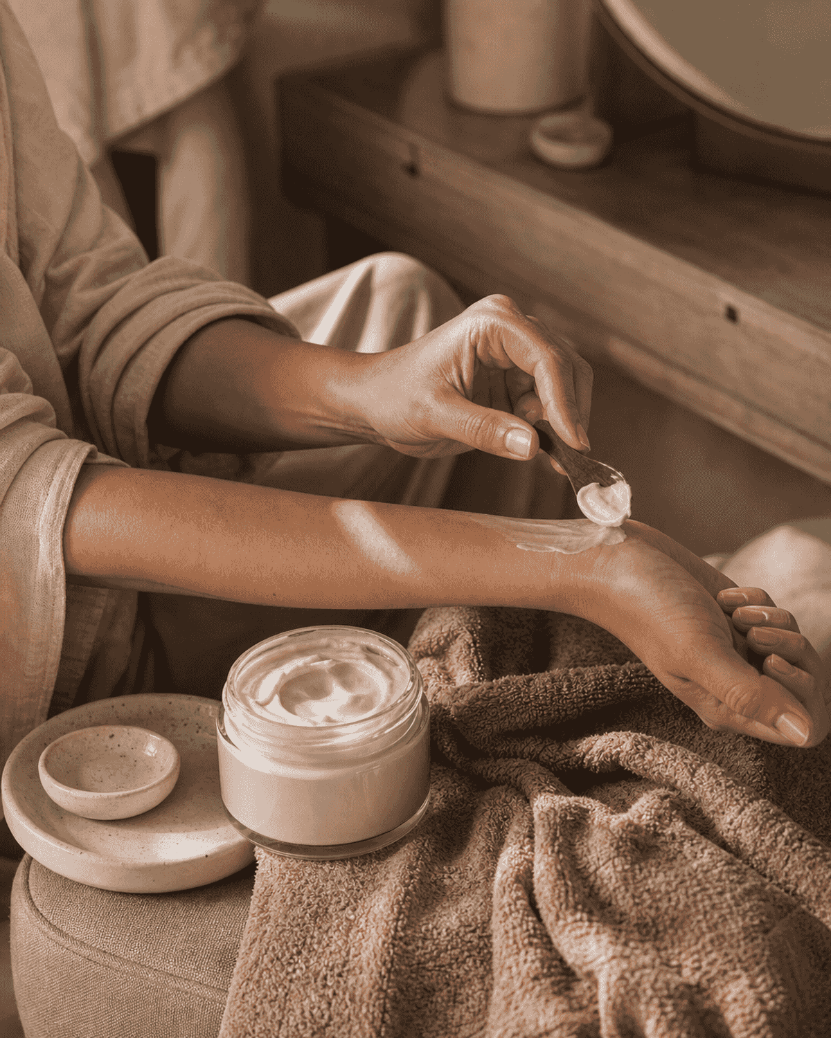 A jar of body cream with a towel and dry brush on warm tile.